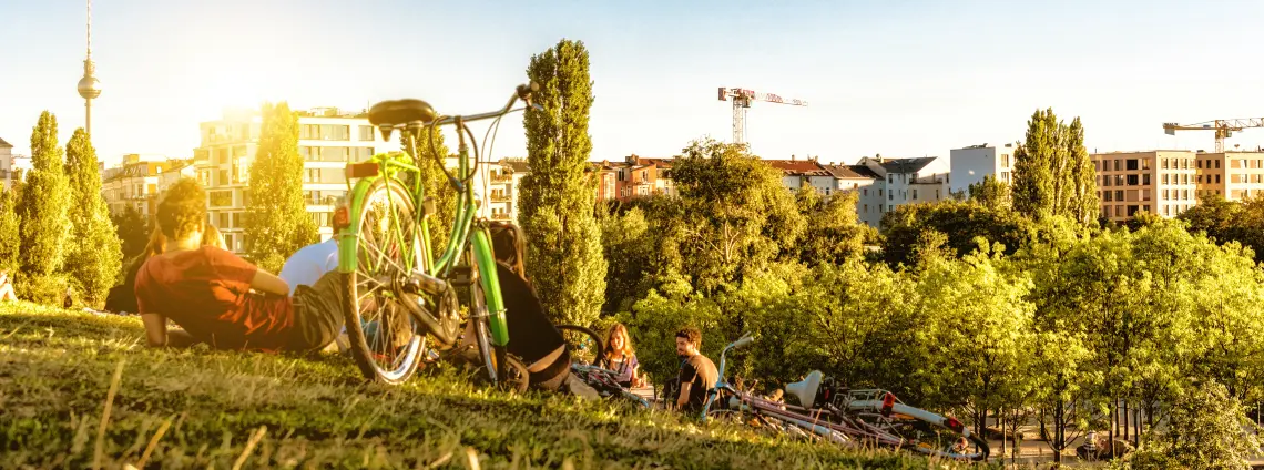 Abendsonne: Personen liegen neben ihren Fahrrädern auf einer Wiese und blicken auf die Skyline von Berlin.