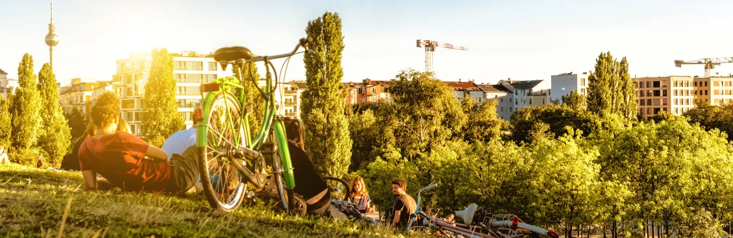 Abendsonne: Personen liegen neben ihren Fahrrädern auf einer Wiese und blicken auf die Skyline von Berlin.