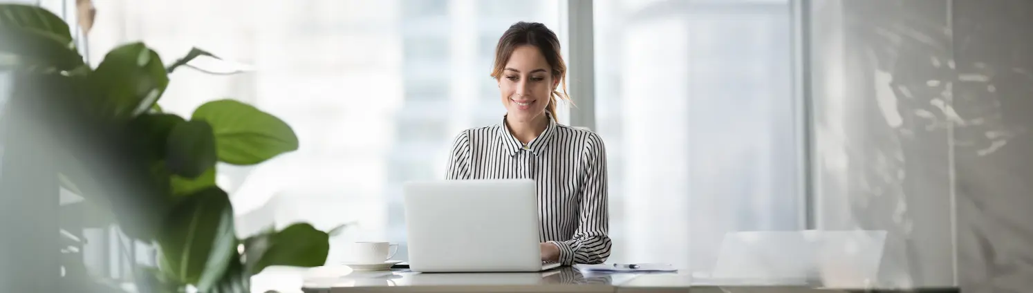 Eine Frau sitzt am Schreibtisch und arbeitet am Laptop