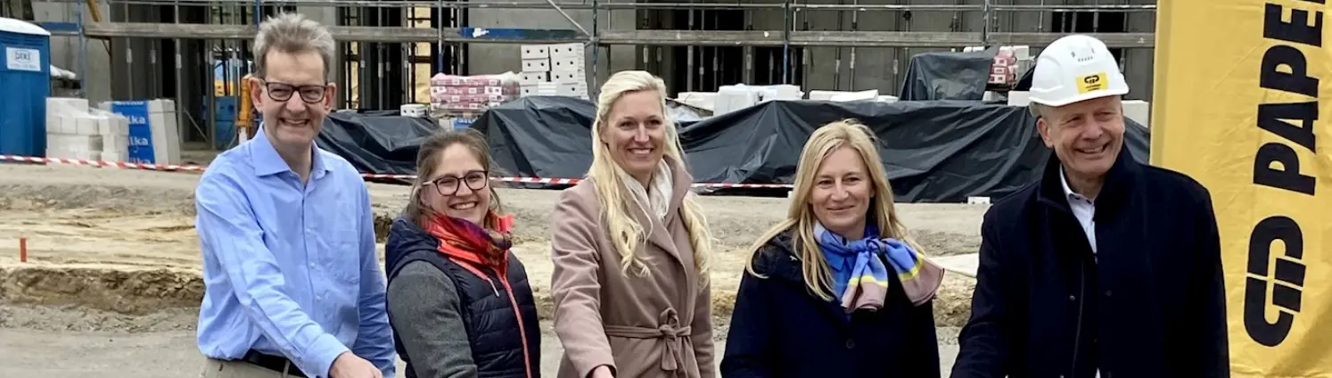 Drei Frauen und zwei Männer stehen auf einer Baustelle und vollführen den symbolischen ersten Spatenstich