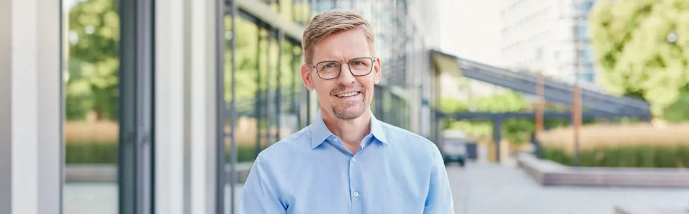 Gunnar Wilhelm, Managing Director der GASAG Solution Plus, steht mit blauem Hemd vor einem Gebäude und lächelt in die Kamera