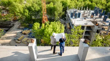 Zwei Personen stehen auf einer Baustelle und schauen aus der Vogelperspektive auf den Rohbau