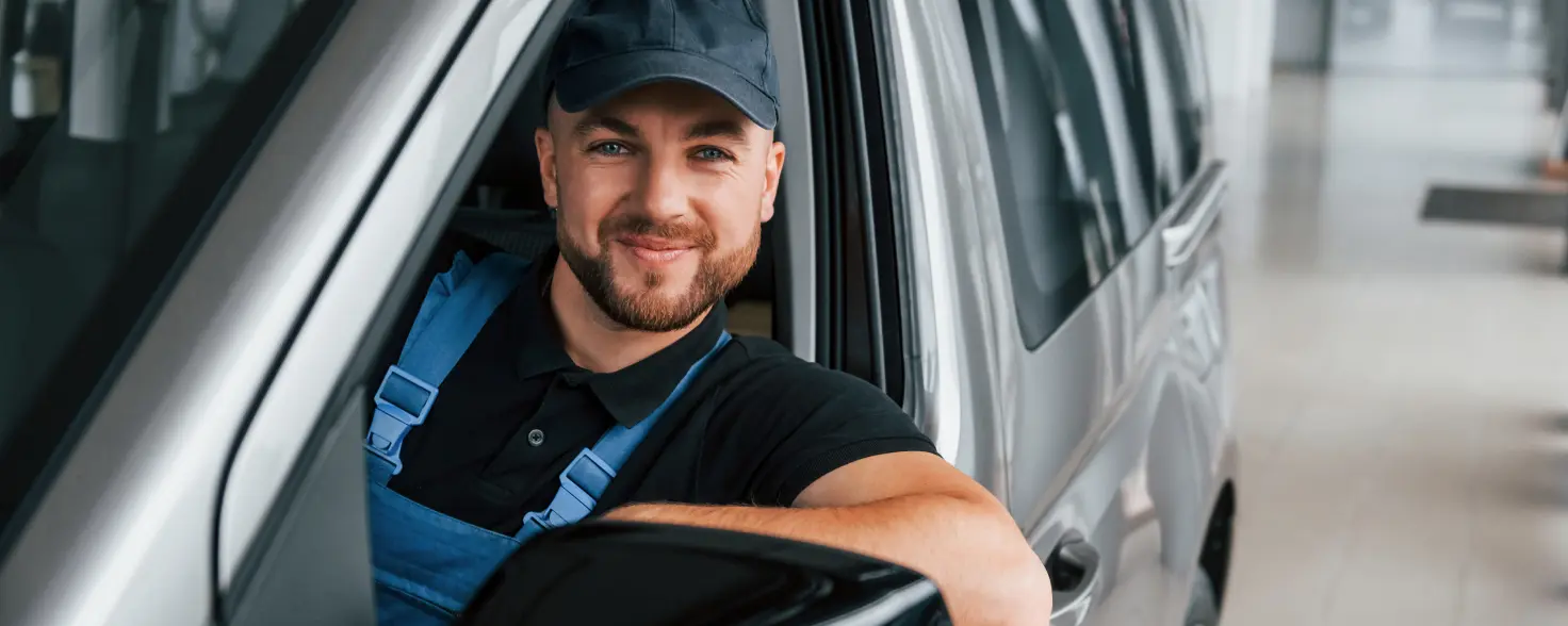 Handwerker sitzt in Elektro-Van und lächelt durch das offene Fenster der Fahrertür.