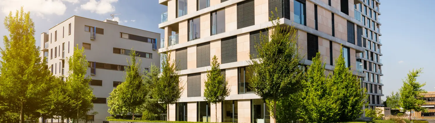 Ein modernes Mehrfamilienhaus vor blauem Himmel mit grünen Bäumen vor dem Gebäude