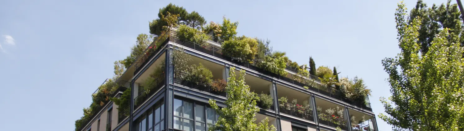 Ein modernes, begrüntes Mehrfamilienhaus mit großen Glasfenstern vor blauem Himmel