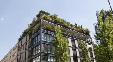 Ein modernes, begrüntes Mehrfamilienhaus mit großen Glasfenstern vor blauem Himmel